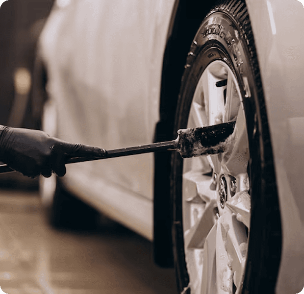 Professional detailer cleaning a car wheel with a brush